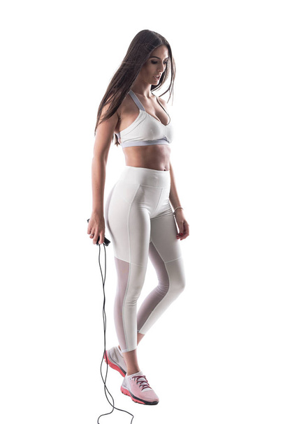 Exhausted sporty woman cardio trainer looking down and holding skipping jump rope. Full body isolated on white background.  - Photo, Image
