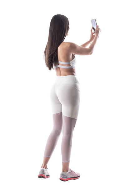 Rückansicht einer sexy Fitness-Frau mit athletischem Körper, die Selfie-Fotos macht. Ganzkörper isoliert auf weißem Hintergrund.  - Foto, Bild