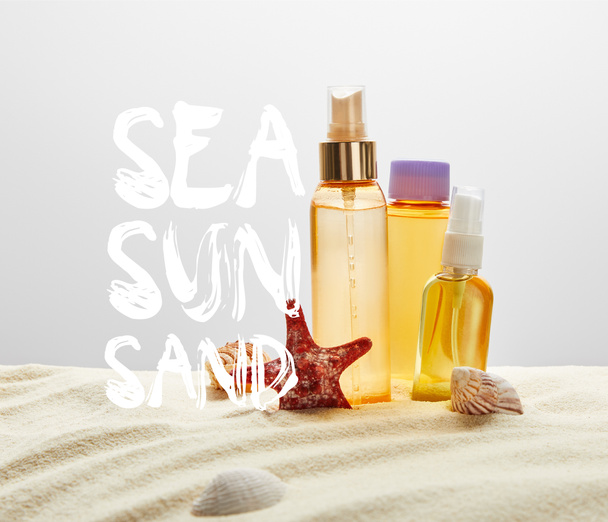 bottles with sunscreen products on sand with starfish on grey background with sea, sun, sand lettering - Photo, Image