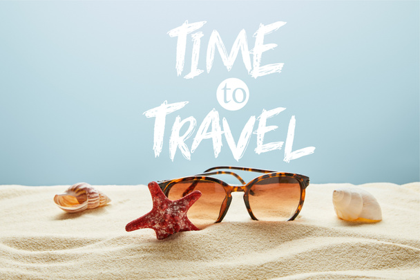 brązowe stylowe okulary przeciwsłoneczne na piasku z muszli i rozgwiazdy na niebieskim tle z czasem do podróży napis - Zdjęcie, obraz