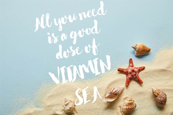 Top uitzicht van zand met schelpen en Starfish op blauwe achtergrond met alles wat je nodig hebt is een goede dosis van vitamine zee belettering - Foto, afbeelding