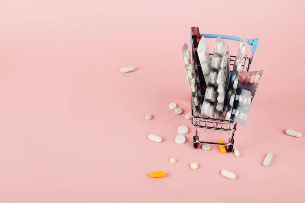 Shopping cart loaded with pills on a pink background. The concep - Foto, Imagem