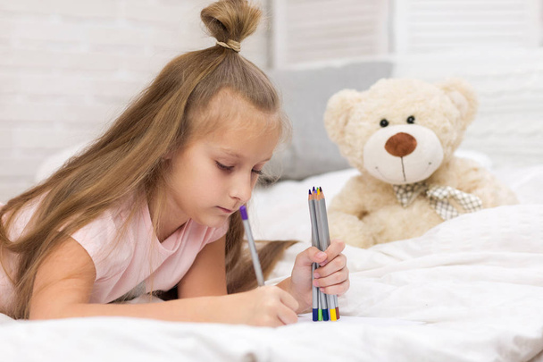 cute little girl drawing pictures while lying on bed - Фото, изображение