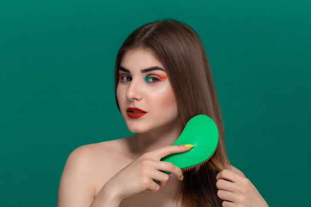 Portrait of beautiful young woman with bright color make-up combing hair with a brush. - Photo, Image