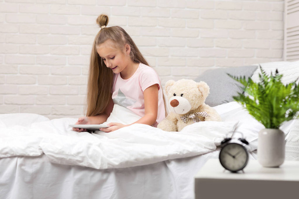 cute little girl lies in bed uses digital tablet. - Photo, Image