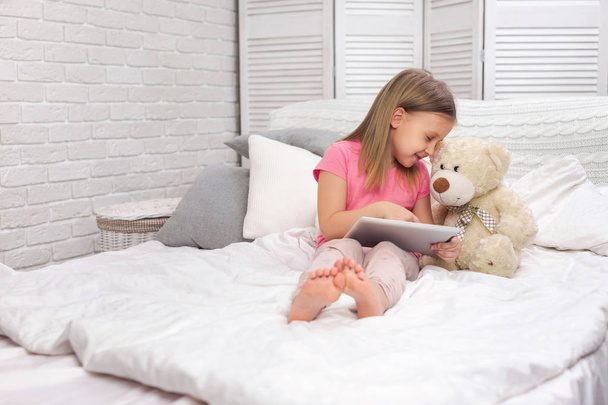 cute little girl lies in bed uses digital tablet. - Фото, зображення
