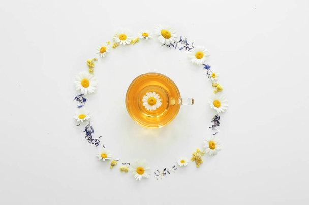 Чашка горячего ромашкового чая и цветы на белом фоне
 - Фото, изображение
