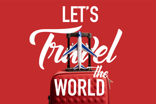 red colorful textured travel bag with plane model isolated on red with lets travel the world illustration - Foto, imagen