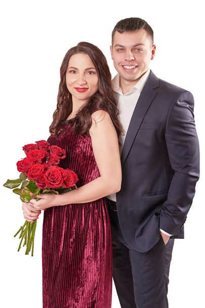 νεαρό παντρεμένο ζευγάρι με ένα μπουκέτο από κόκκινα τριαντάφυλλα σε μπεζ φόντο στις 14 Φεβρουαρίου στην ημέρα του Αγίου Βαλεντίνου - Φωτογραφία, εικόνα
