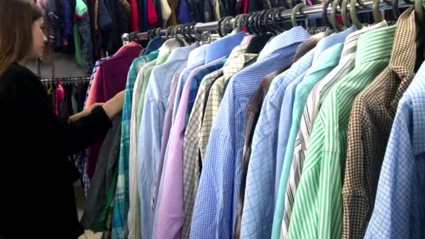 Κοντινό χέρι γυναίκα στο κατάστημα κοιτάζει μέσα από σακάκια και πουκάμισα, τα οποία κρέμονται στα ράφια - Πλάνα, βίντεο