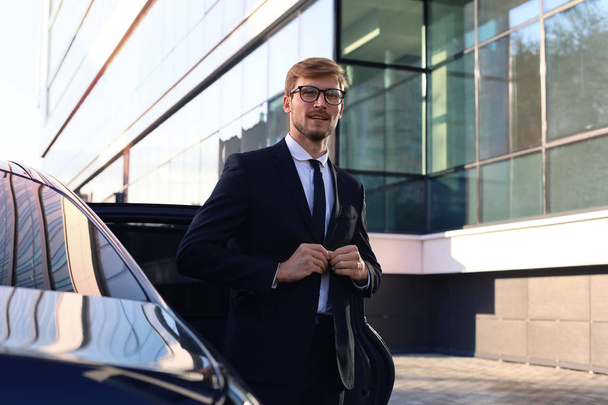 Handsome serious young businessman standing near his comfortable new car and going to the office. - Zdjęcie, obraz