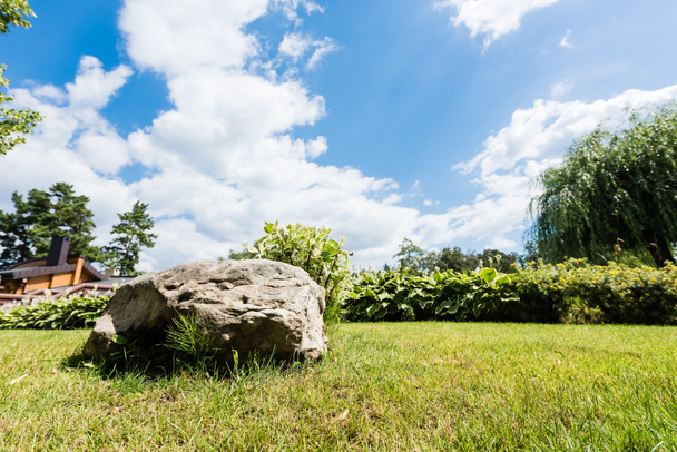 selective focus of rock on green grass against blue sky with clouds  - Photo, Image