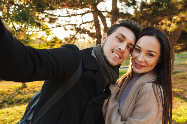 Happy young beautiful loving couple posing walking outdoors in park nature take selfie by camera. - Photo, Image
