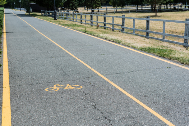 Gelbes Symbol des Radweges auf grauem Asphalt neben Zaun  - Foto, Bild