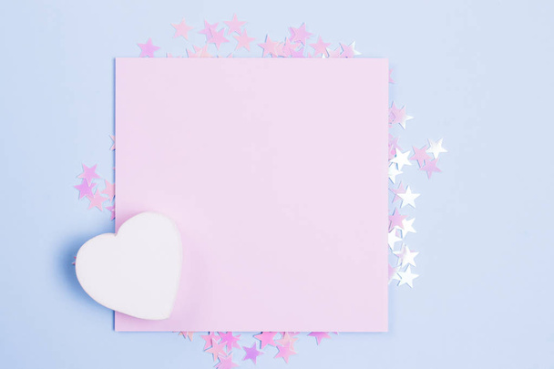 Pastel pink blank card mockup and white wooden heart on pastel blue background with scattered pink glitter stars. Place for your text. Gbar style. - Foto, Bild