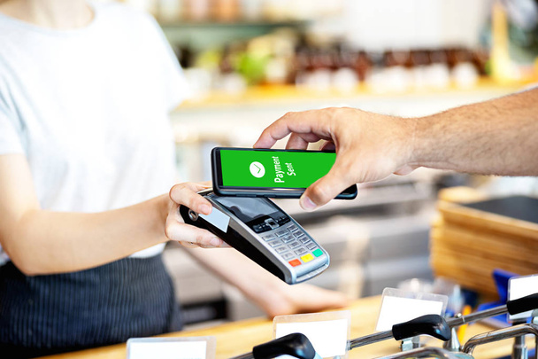 Σερβιτόρα Holding συσκευή ανάγνωσης καρτών για τον άνθρωπο που πληρώνει με smartphone στο κατάστημα, πελάτης χρησιμοποιώντας το κινητό τηλέφωνο για την πληρωμή, ιδέα της μικρής επιχειρηματικής υπηρεσίας με ταμία αποδοχή συναλλαγής μέσω της τεχνολογίας NFC. - Φωτογραφία, εικόνα