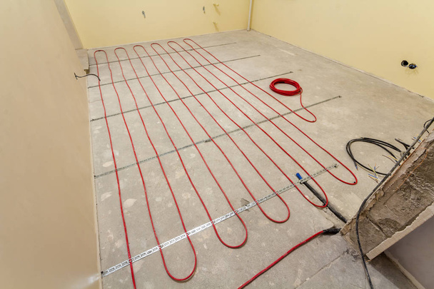 Calefacción instalación de cable eléctrico rojo en el suelo de cemento en una pequeña habitación nueva sin terminar con paredes enlucidas. Renovación y construcción, cómodo concepto de hogar cálido
. - Foto, Imagen