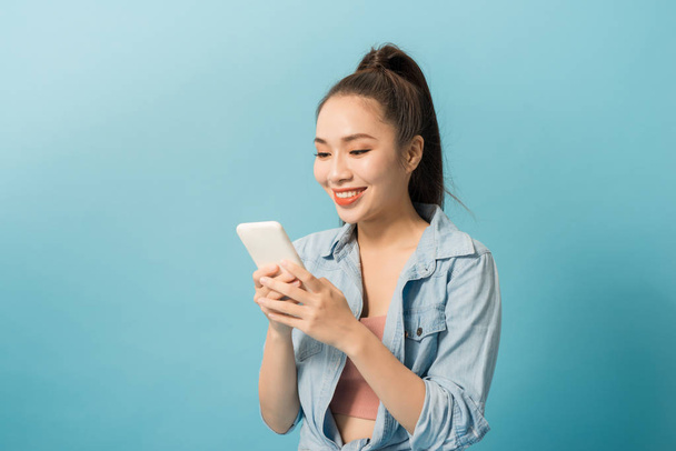 Aasialainen nainen 20s tilalla matkapuhelin ja hymyilee sinisellä taustalla
 - Valokuva, kuva