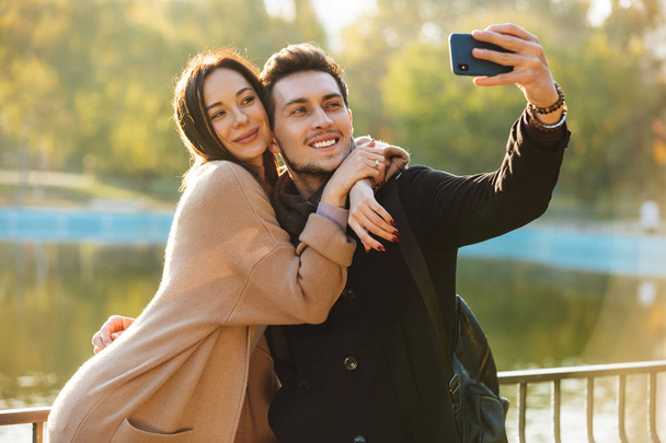 Szczęśliwy młody piękny kochający para pozowanie chodzenie na dworze w Park natura brać selfie przez zdejmowany telefon. - Zdjęcie, obraz