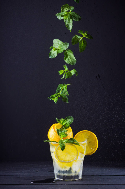 Lemonade with flying mint and lemon. Summer refreshing drink with lemon on dark background. Infused water with citrus and mint. Summer cocktail in a spray of water. Levitation - Foto, Imagem