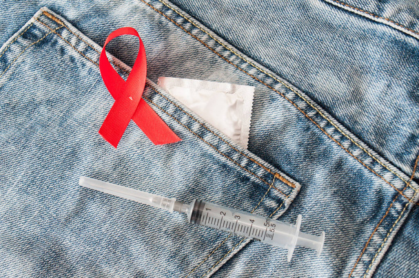 Jeringa de cinta roja y condón en jeans. Día Mundial del SIDA. - Foto, Imagen