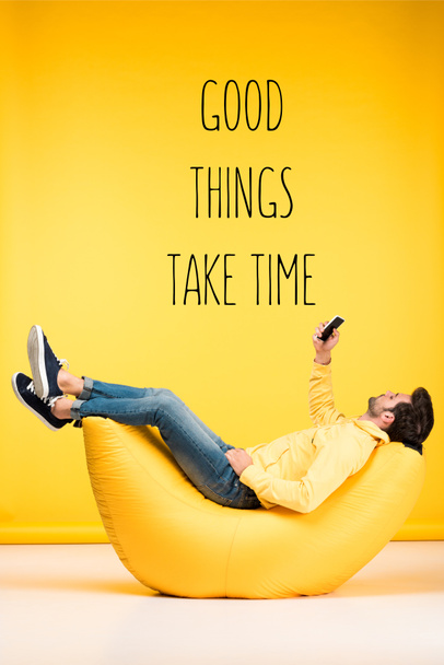 man relaxing on bean bag chair and using smartphone on yellow background with good things take time inspiration - Photo, Image