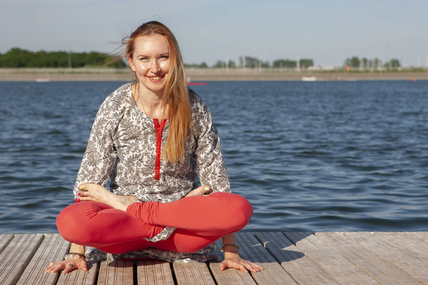 An image of a pretty woman doing yoga at the lake - Фото, изображение