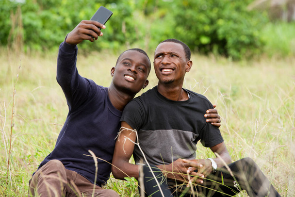 dois jovens usando telefone celular sentado na grama
 - Foto, Imagem