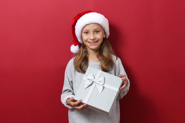 carino allegro ragazza in un cappello di Natale su uno sfondo colorato in possesso di un regalo - Foto, immagini