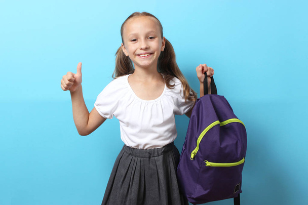 Χαριτωμένη χαμογελαστή μαθήτρια με σχολική τσάντα σε έγχρωμο φόντο. Επιστροφή στο σχολείο έννοια - Φωτογραφία, εικόνα