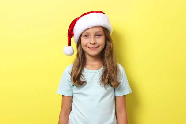χαρούμενο κορίτσι σε ένα έγχρωμο φόντο στο καπέλο των Χριστουγέννων - Φωτογραφία, εικόνα