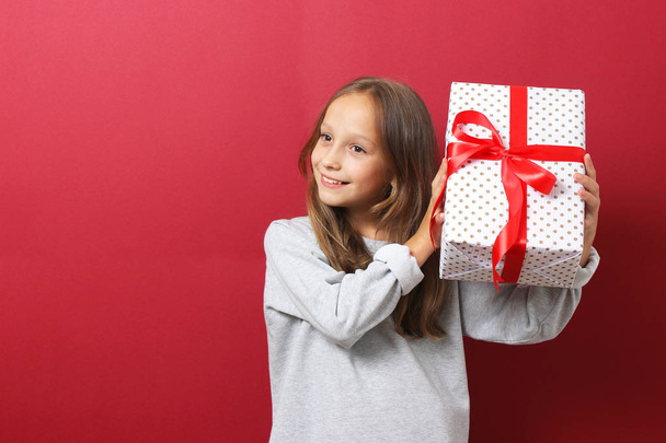 schattig vrolijk meisje in een kerst hoed op een gekleurde achtergrond met een geschenk - Foto, afbeelding