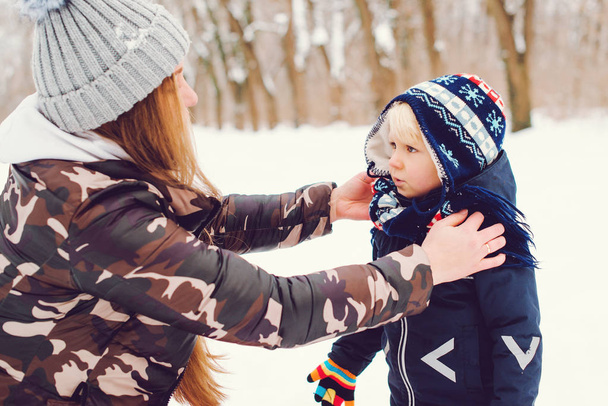 Nuori äiti ja hänen poikavauvansa talvikävelyllä. Talvi luminen sää. Onnellinen lapsi yllään talviasu kylmänä päivänä
. - Valokuva, kuva