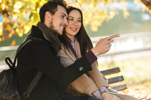 Happy young beautiful loving couple posing walking outdoors in park nature sitting on bench. - 写真・画像
