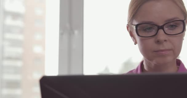 Portrait of smiling woman wearing glasses working at home with a laptop - Záběry, video