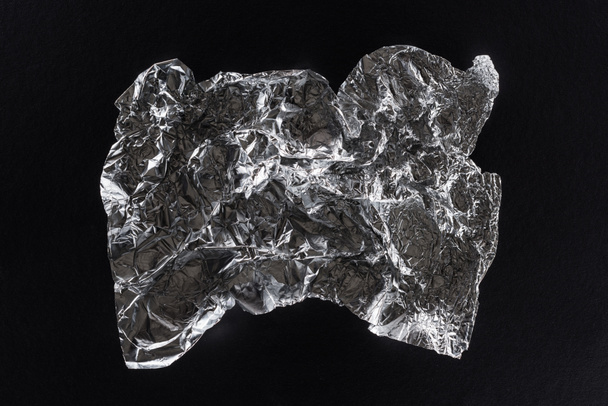 top view of glossy crumpled silver foil isolated on black - Foto, imagen