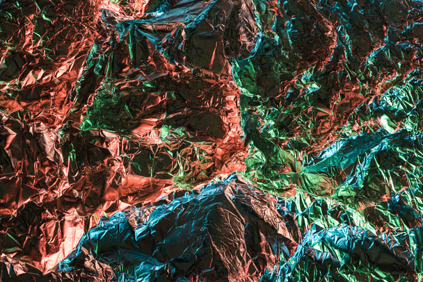 top view of glossy textured crumpled foil with colorful lighting reflection in darkness - Foto, Imagen