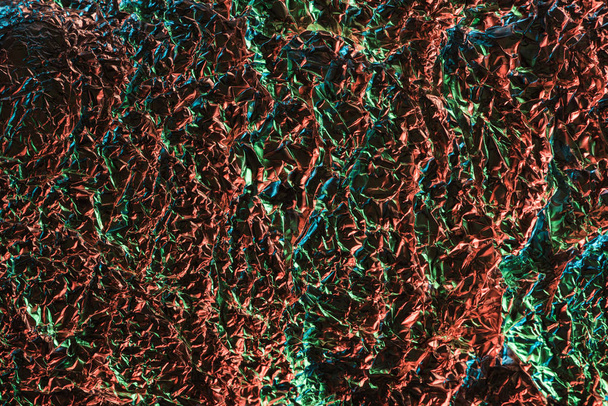 top view of textured crumpled foil with colorful lighting in darkness - Foto, imagen