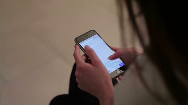 video, které sedí na podlaze a drží smartphone v dlaních, dívku hledající ve smartphone nějaké informace v kontaktech - Záběry, video