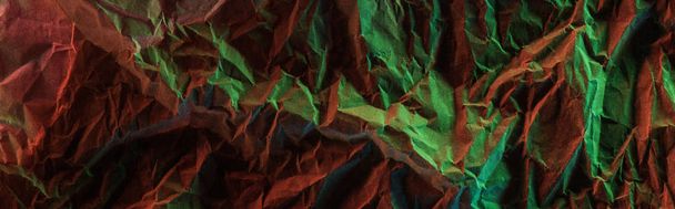 panoramic shot of crumpled paper with green colorful lighting in darkness - 写真・画像