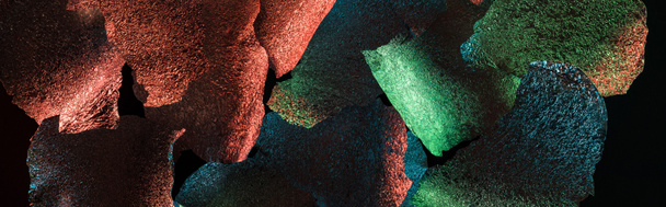panoramische foto van abstracte achtergrond van gescheurde folie met kleurrijke verlichting geïsoleerd op zwart - Foto, afbeelding