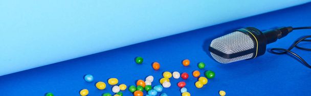 panoramic shot of black microphone with candies on colorful background  - Photo, Image