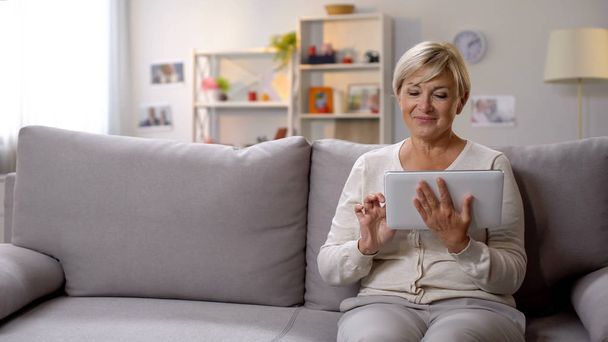Aged female using tablet, surfing net, leisure time spending, social media - Foto, Imagen