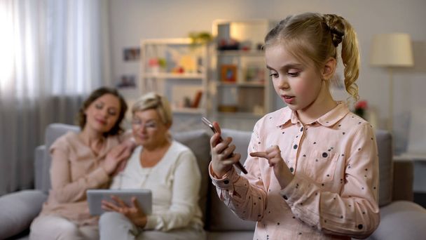 Pretty child using smartphone app, grandmother and mother scrolling tablet - Fotoğraf, Görsel
