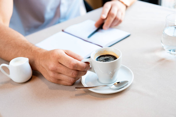 partial view of man holding cup of coffee while sitting in cafe with textbook and pen - Foto, immagini
