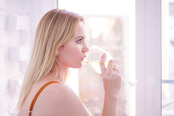 かなりプラスサイズの白人女性は、白い毛皮の窓ガラスの上に自宅で一人で朝にワインを飲みます  - 写真・画像