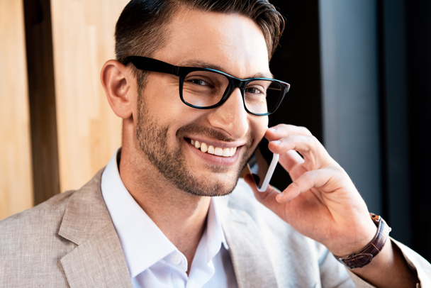 smiling businessman in glasses talking on smartphone in cafe - Фото, изображение