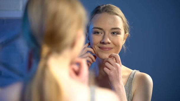 Young smiling lady looking at mirror reflection, happy with skin treatment - Valokuva, kuva