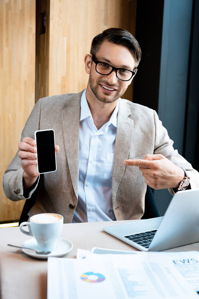 businessman pointing with finger at smartphone with blank screen in cafe - Foto, Bild