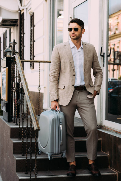 full length view of business man in sunglasses holding suitcase on street - Foto, Bild